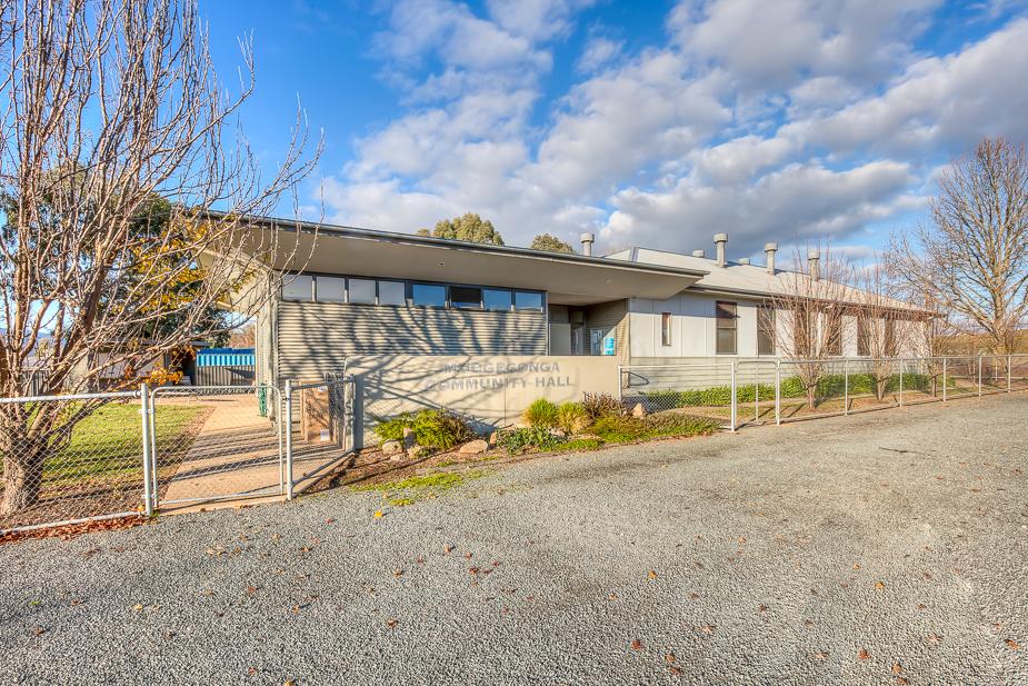 the exterior of Mudgegonga Community Hall, a single-story building clad in Colourbond. There is a short chain-link fence bordering the Hall.