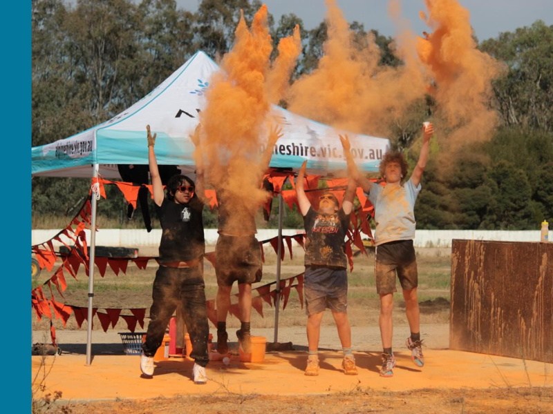 Four teenagers throwing orange coloured powder into the air at the 2024 Colour Fun Run in Myrtleford.