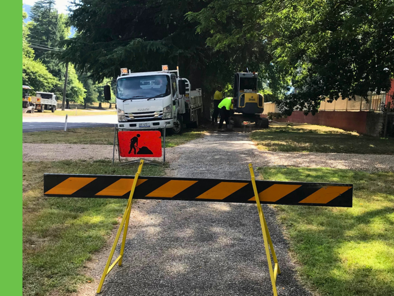 Footpath closed off with yellow and black barrier to indicate path is closed. Truck and workman in background.