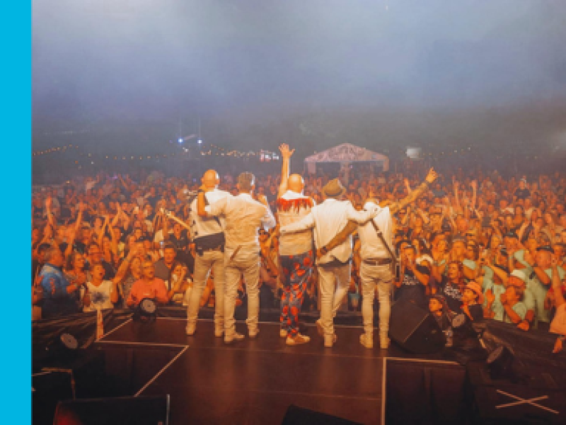 Performers on stage facing a large crowd and waving